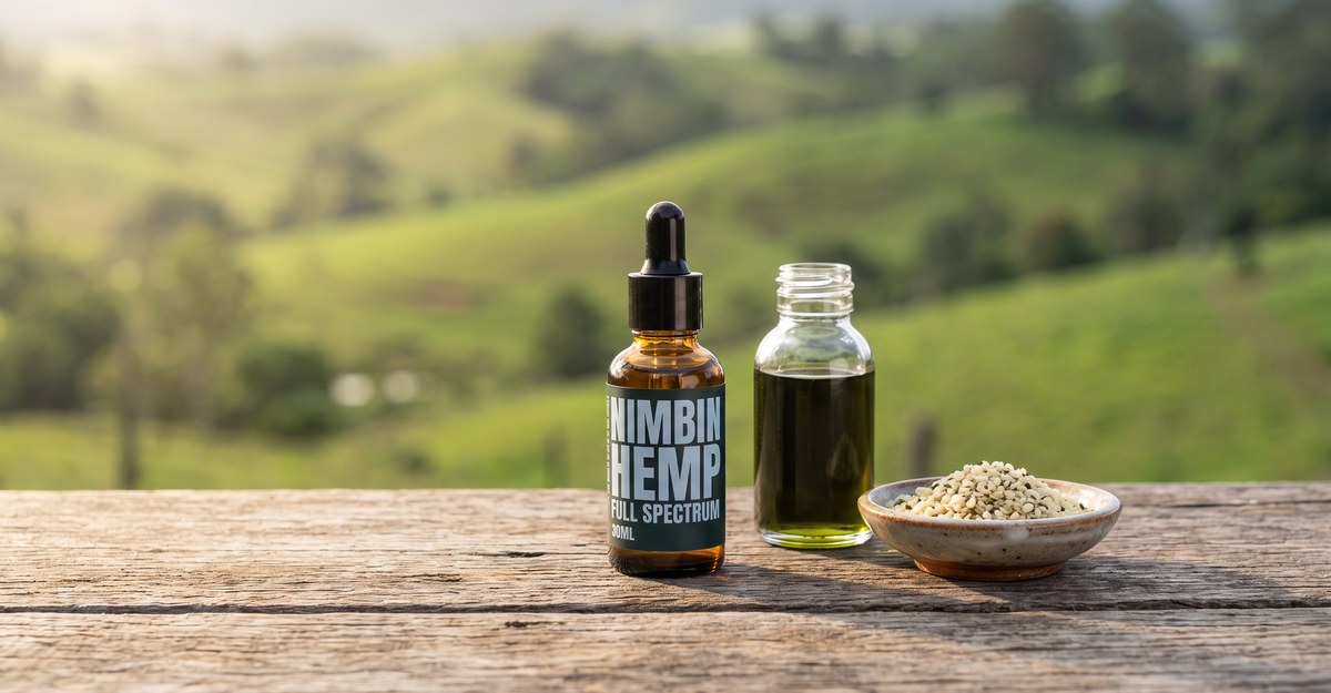 Nimbin Hemp full spectrum hemp oil bottle beside a jar of hemp seed oil and a bowl of hulled hemp seeds on a timber bench, green hills behind